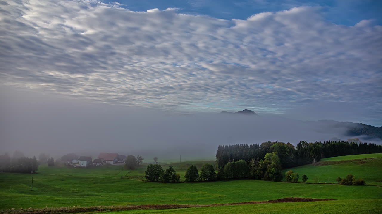 아침 일찍 안개 층에 화려한 건물과 함께 그림 같은 초원과 함께 오스트리아 풍경의 타임  ⁇ 스 언덕과 산의 전망과 함께 빠르게 움직이는 구름