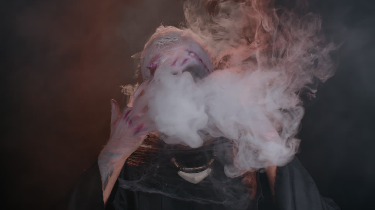 hombre aterrador halloween zombie sangriento herido escondiéndose detrás de las manos sopla humo de la nariz y la boca