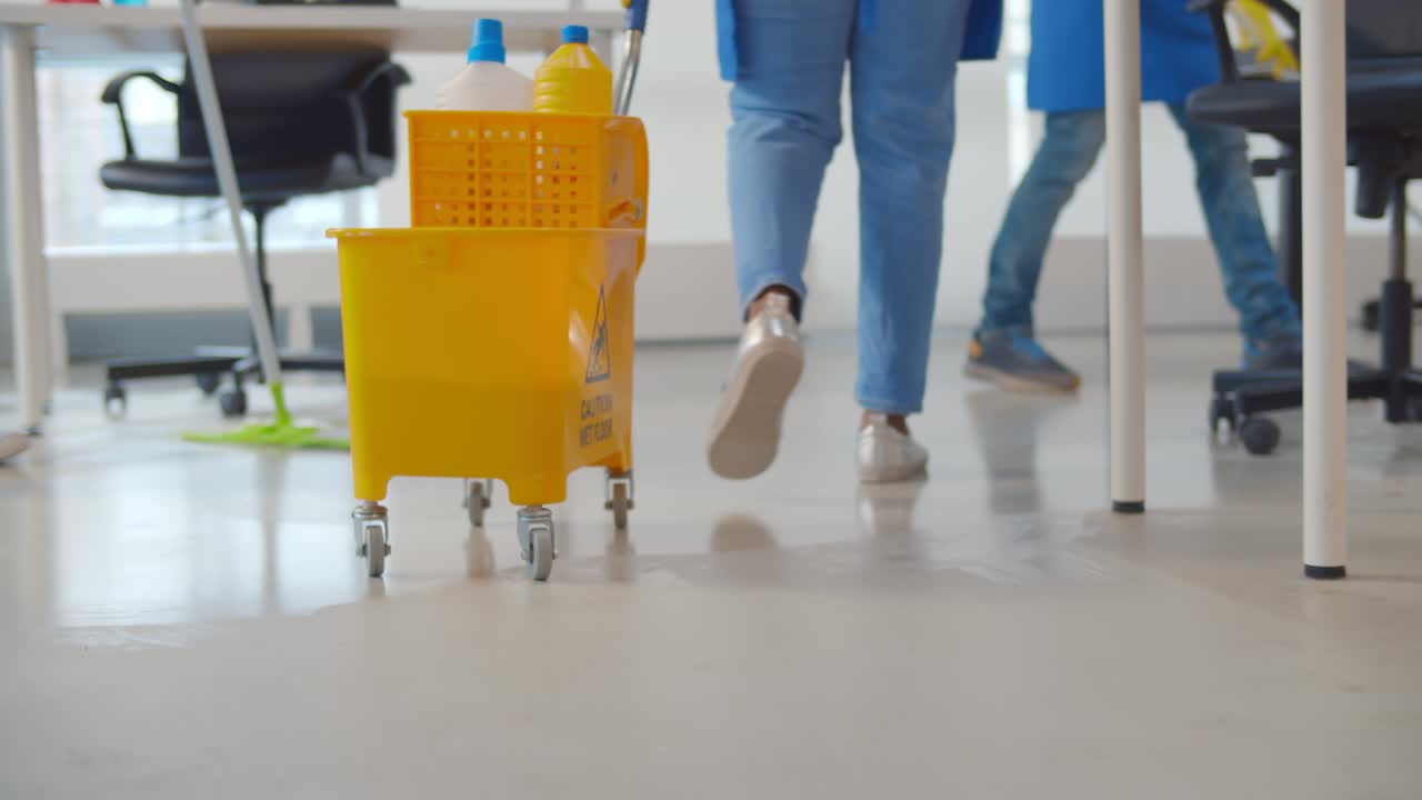 cerca del conserje empujando el carro amarillo y los colegas limpiando el suelo