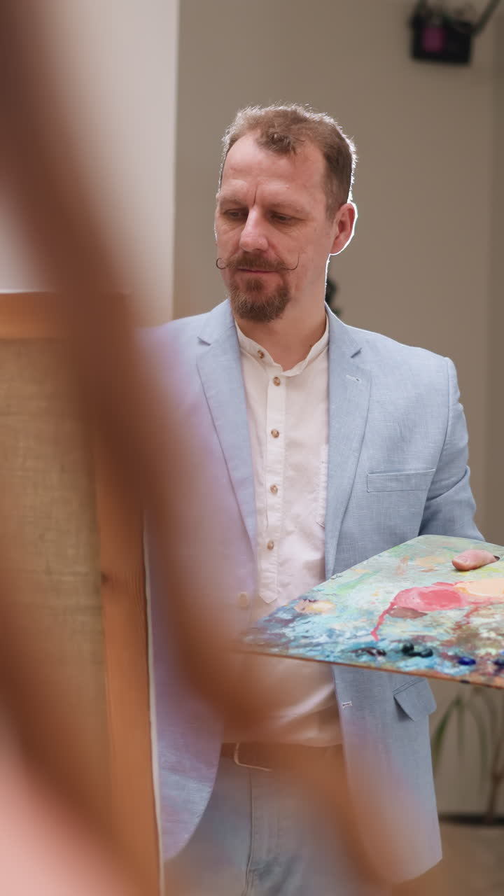 Il pittore osserva il dipinto della modella sulla tela. L'artista professionista dipinge una giovane donna con colori vivaci nello studio d'arte. Visione unica della pittura di ritratto.