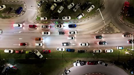 cars lineup at traffic light crowded with vehicles parked on grass median, aerial top down at night