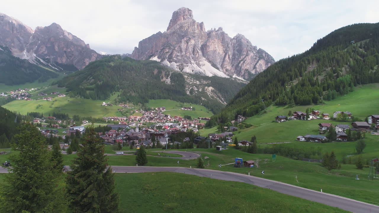Cyclist on a Mountain Road in the Dolomites, Italy, with a Small Town in the Background, from a Drone