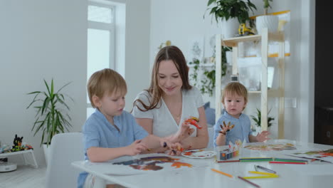 the family has fun painting on paper with their fingers in paint. mom and two children paint with fingers on paper