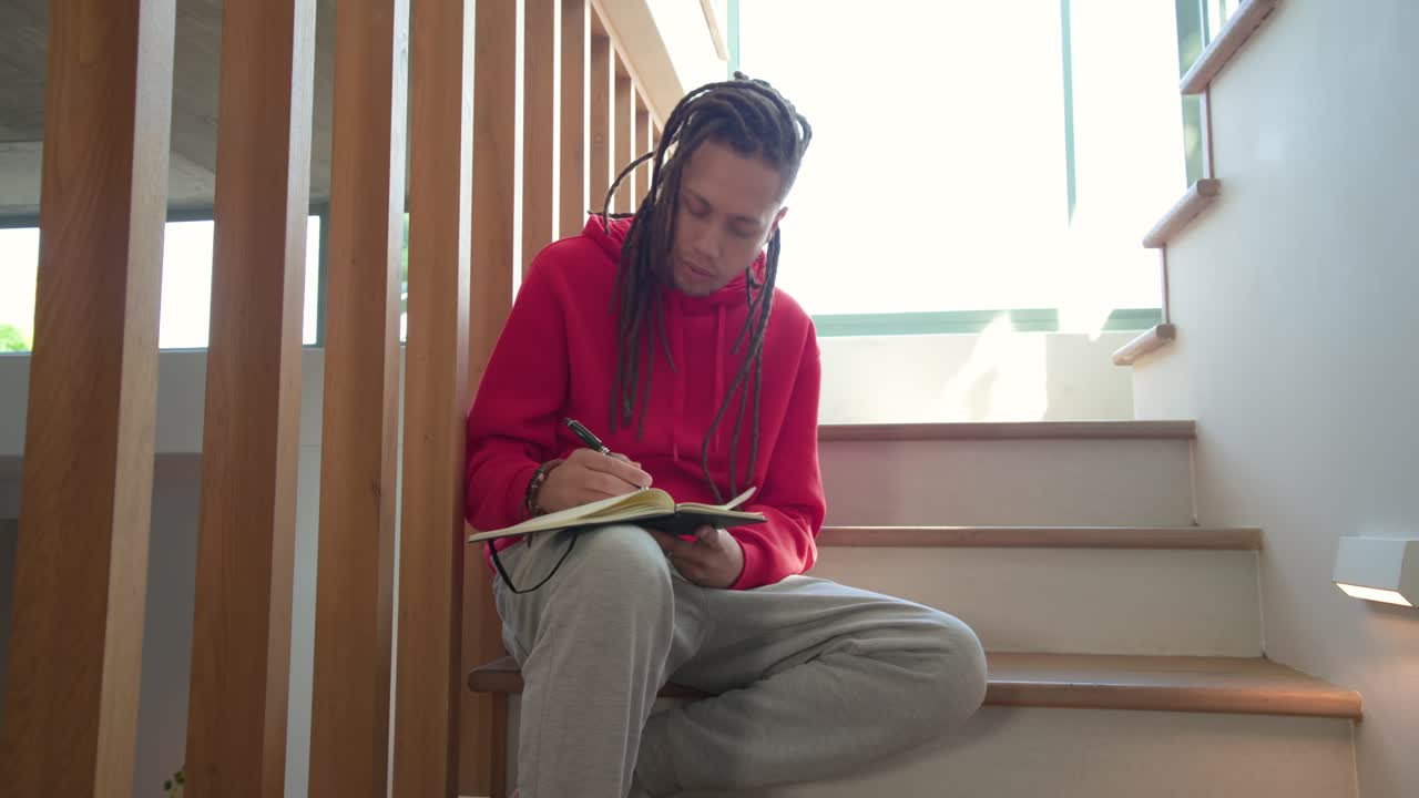 Middelbare man die op een trap een notitieboek opent met een pen, gedachten opschrijft en reflecteert bij het licht van het raam