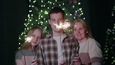 A-happy-family-celebrates-the-new-year-at-the-Christmas-tree,-holding-burning-sparklers