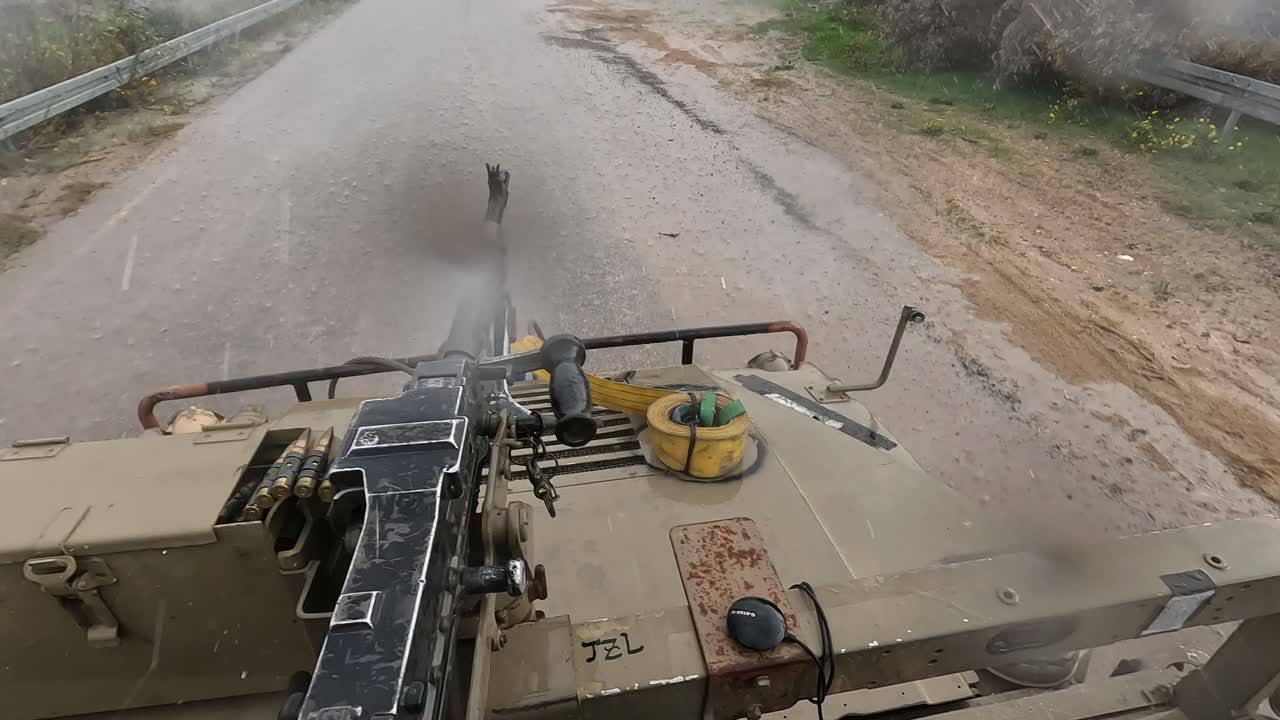 Striscia di Gaza — POV da un veicolo militare che percorre una strada rurale bagnata durante la pioggia mentre un soldato tiene e mangia un panino accanto a un'arma montata