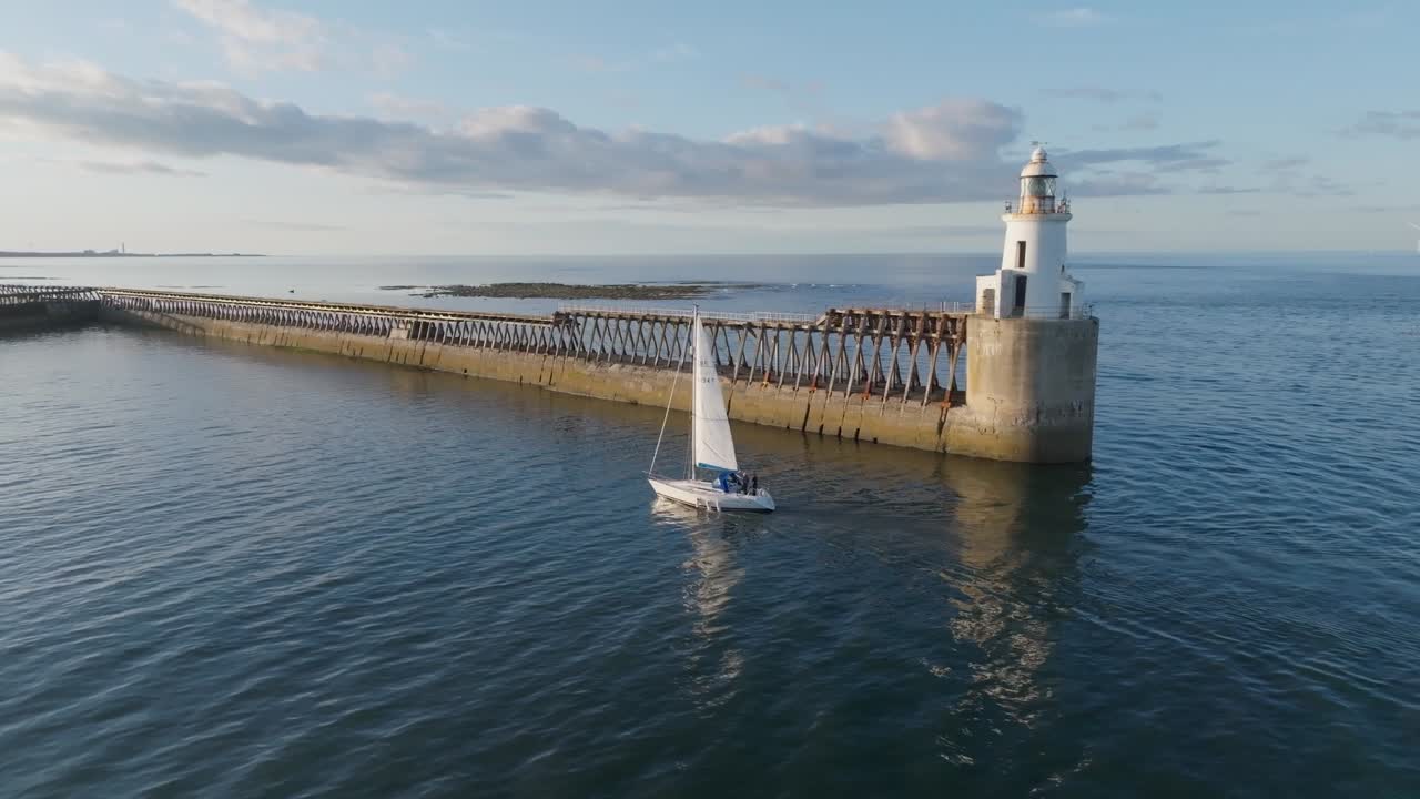 White yacht sailing past white lighthouse on calm summer day