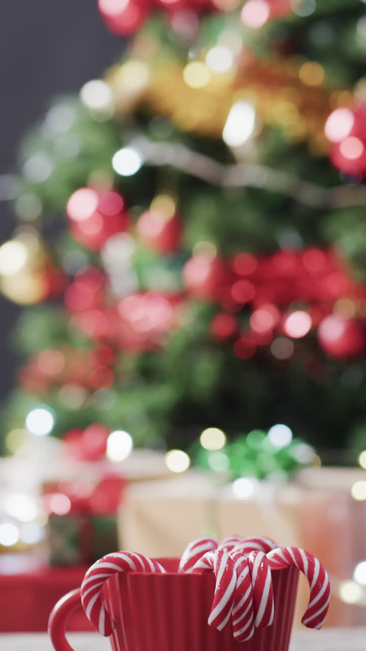 Vertical video of christmas candy canes in mug, christmas tree and copy space