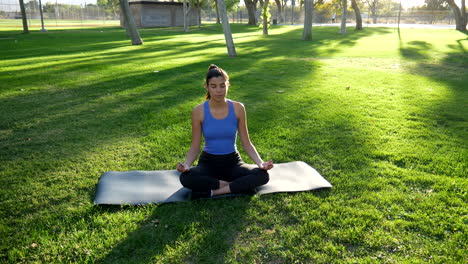 Eine-Schöne-Junge-Hispanische-Frau-Meditiert,-Während-Sie-Bei-Sonnenaufgang-In-Der-Natur-Auf-Einer-Yogamatte-Sitzt