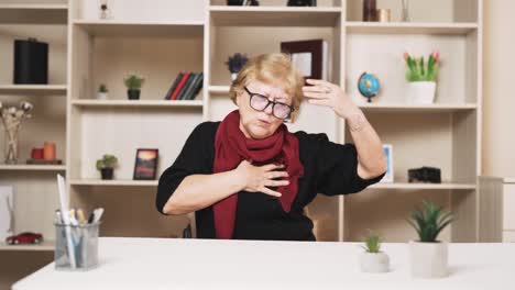 old woman sitting at the table clutches her chest with her hands and begins massaging during a heart attack