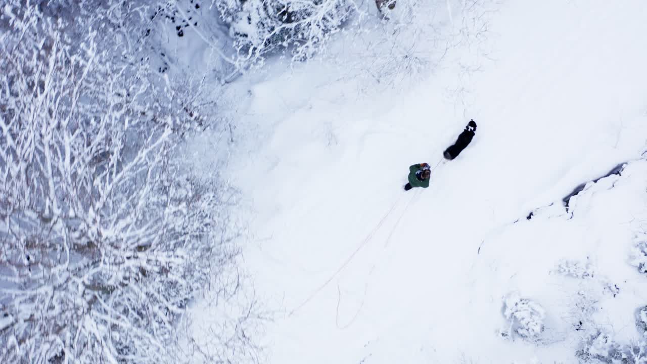 hombre y perro caminando en un sendero forestal helado en invierno - toma aérea