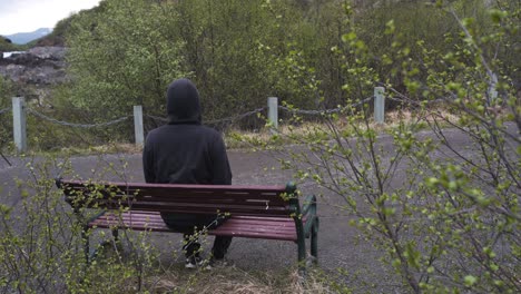 Un-Hombre-Con-Una-Sudadera-Con-Capucha-Sentado-Solo-En-Un-Banco-Solo,-Pensando-En-La-Vida