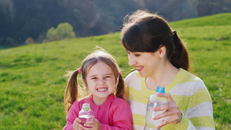 a funny girl of 3-4 years with her lovely mother drinks water the sun's rays illuminate them on a gr