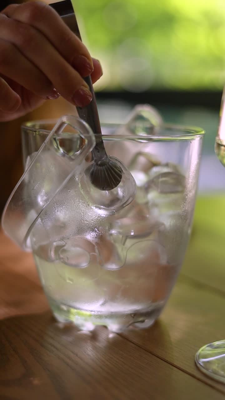 Woman using ice tongs to put ice in a glass ice bucket.