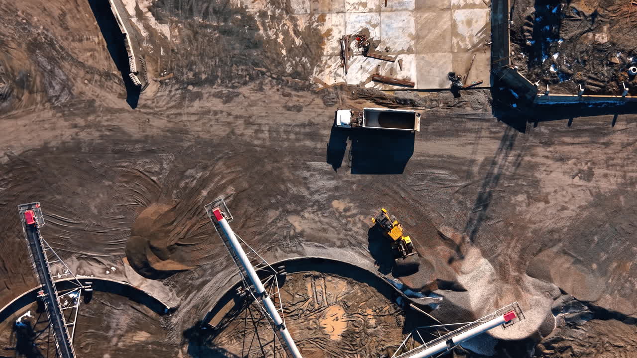 Vertical top view of conveyor belts at stone processing site. Nadir aerial shot of industrial machinery and aggregate stockpiles on the ground