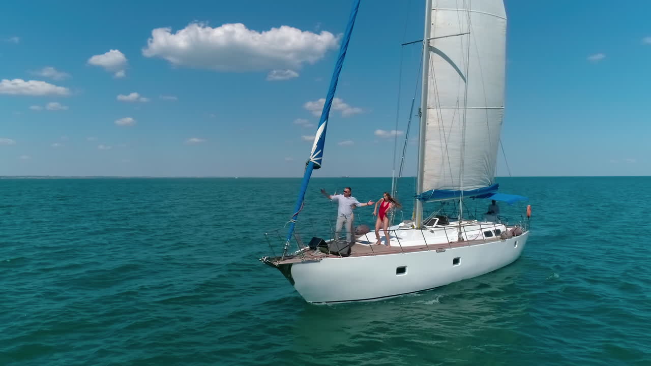 Luxury cruise on the open sea. White sailboat floating on blue water in a bright summer day. Young people resting on yacht. Musical group performing music on ship.