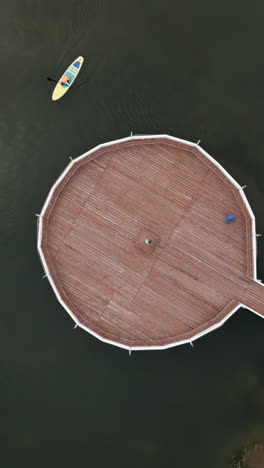 circular wooden platform on a lake with paddleboard