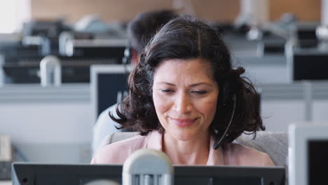 Mature-Businesswoman-Wearing-Telephone-Headset-Talking-To-Caller-In-Customer-Services-Department