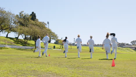 playing cricket, women in white uniforms practicing on grassy field