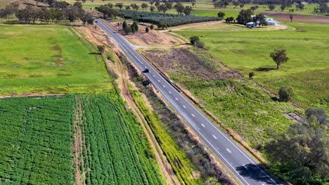 drone footage captures a straight rural road cutting through green fields and rolling hills under bright daylight, with minimal traffic and stable overhead perspective