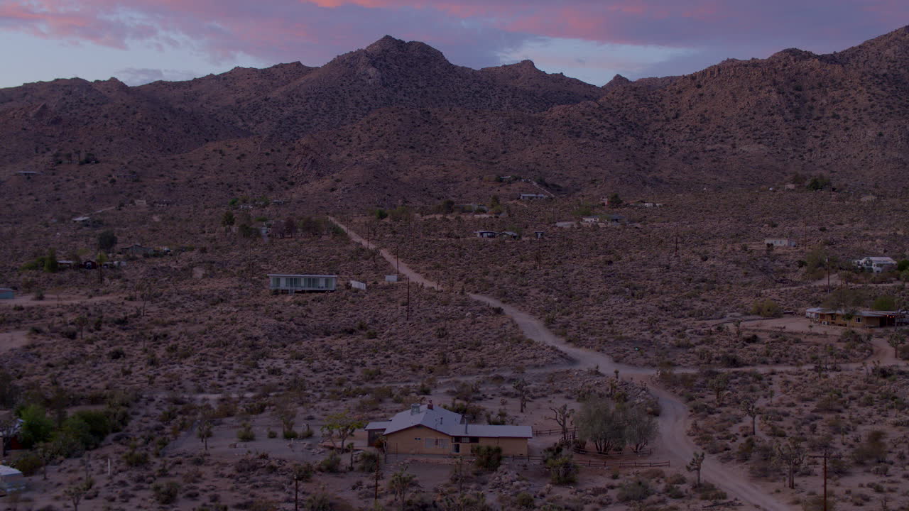 Lenta ascesa sopra case e una vecchia strada sterrata solitaria al tramonto a Joshua Tree, California