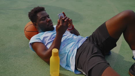 man resting on basketball court, using smartphone