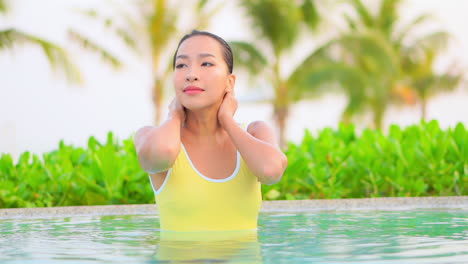 Beautiful-young-woman-in-pool-with-yellow-swimsuit-strokes-wet-hair