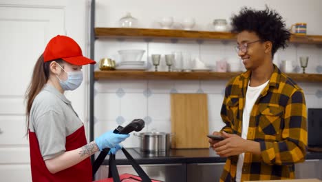 happy african-american man taking pizza from courier and paying with nfc on mobile phone