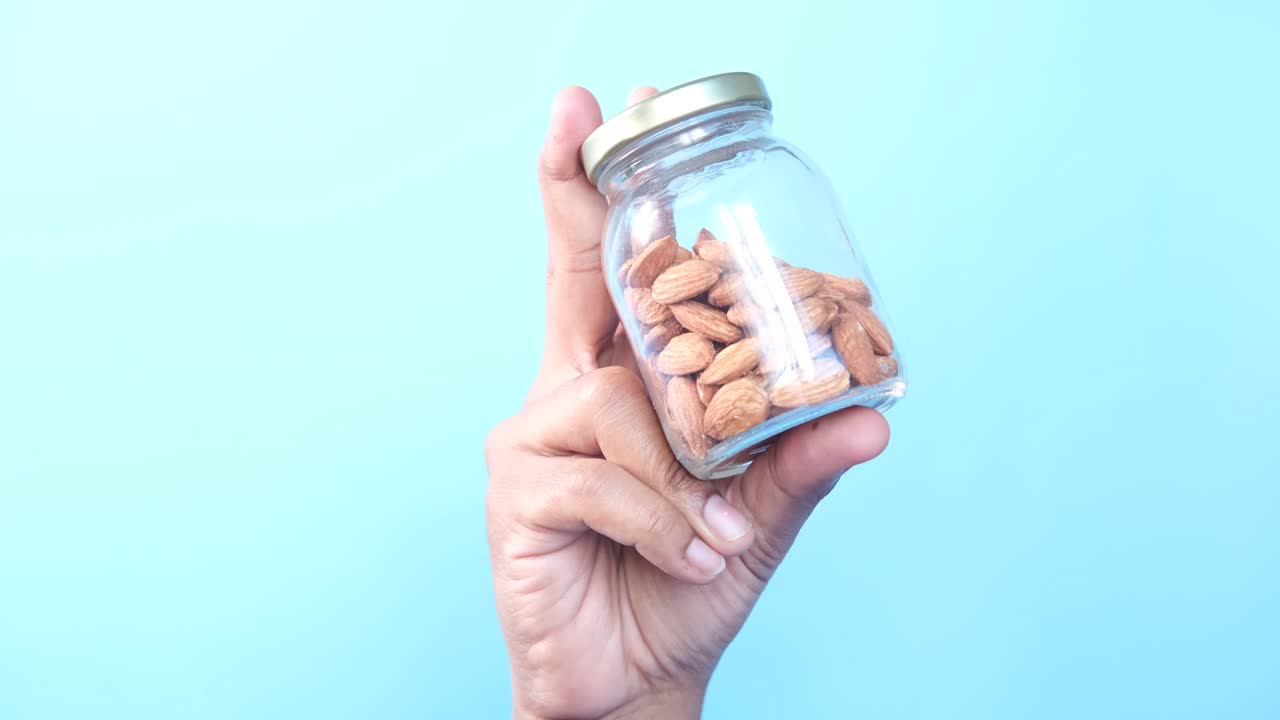mano sosteniendo un frasco de vidrio lleno de almendras