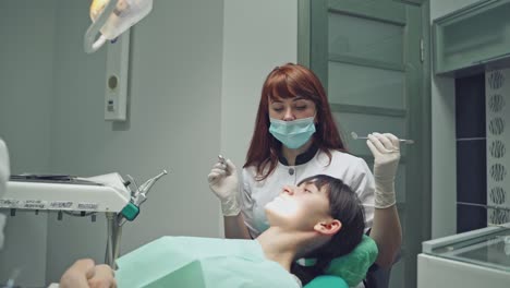 beautiful dentist treating teeth to a woman patient in clinic over dental equipment background. female professional doctor stomatologist at work.
