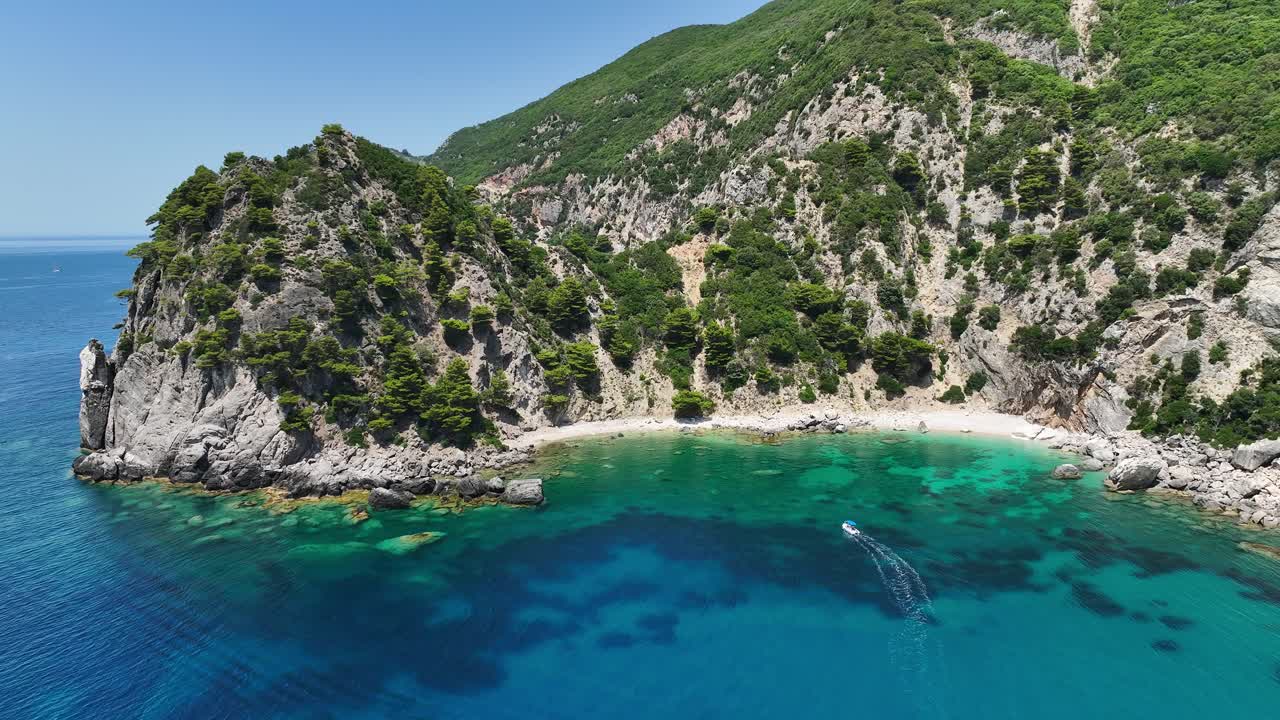 Motoscafo che naviga vicino alle scogliere lussureggianti dell'isola di Corfù sul Mar Ionio turchese, giornata di sole, vista aerea.