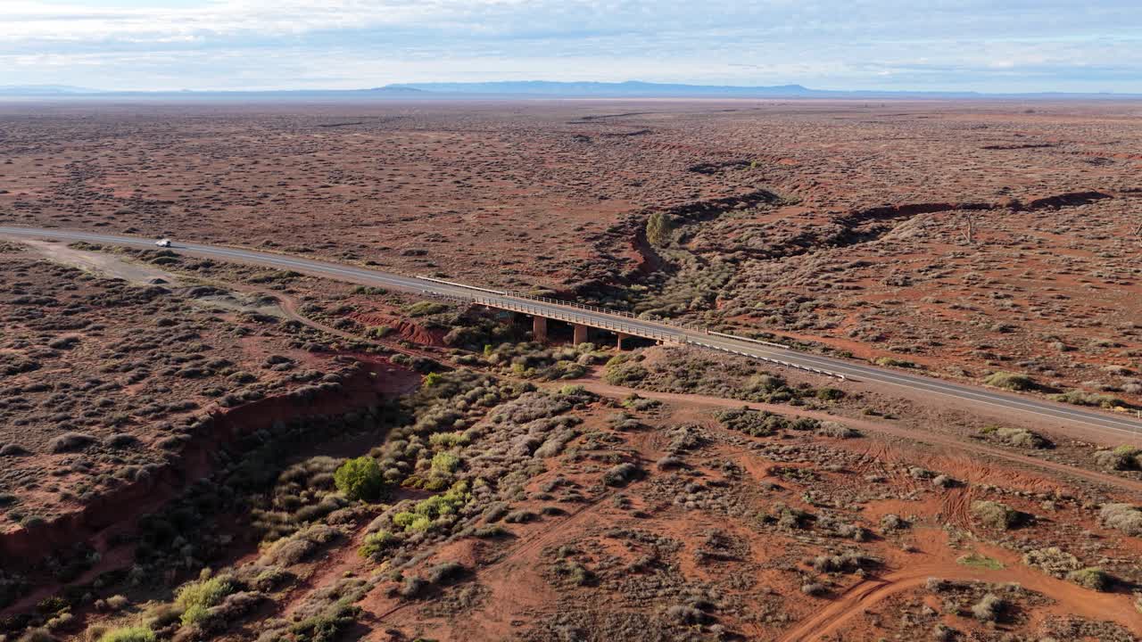 Aerial drone view of white car crossing road bridge in dry outback in South Australia