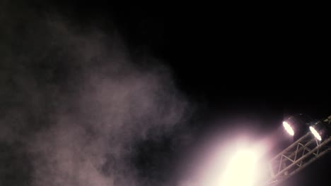 cameras move in slow motion, from the bottom to the top facing a drum set in the stage at an outdoor concert while stage lights are moving and stage smoke is around