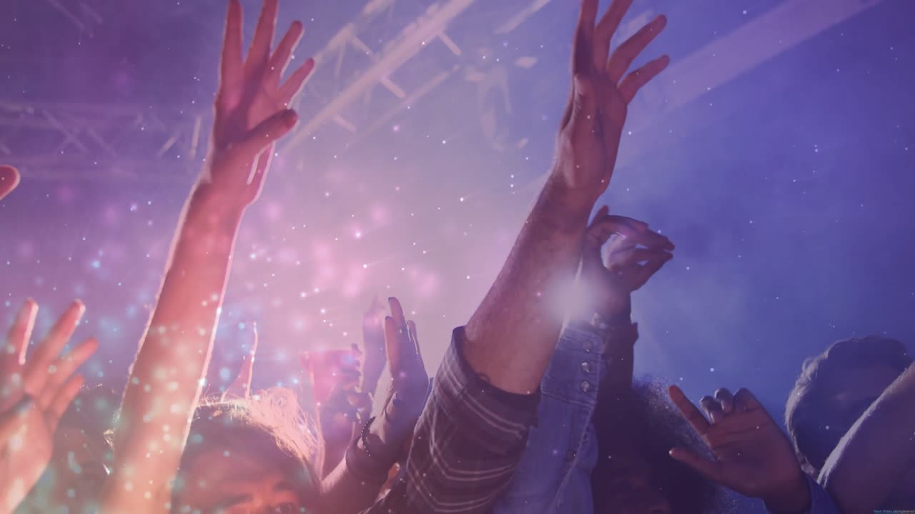 Un 'beat drop' impulsa a la multitud de música a levantar las manos y animar bajo luces moradas con confeti girando.