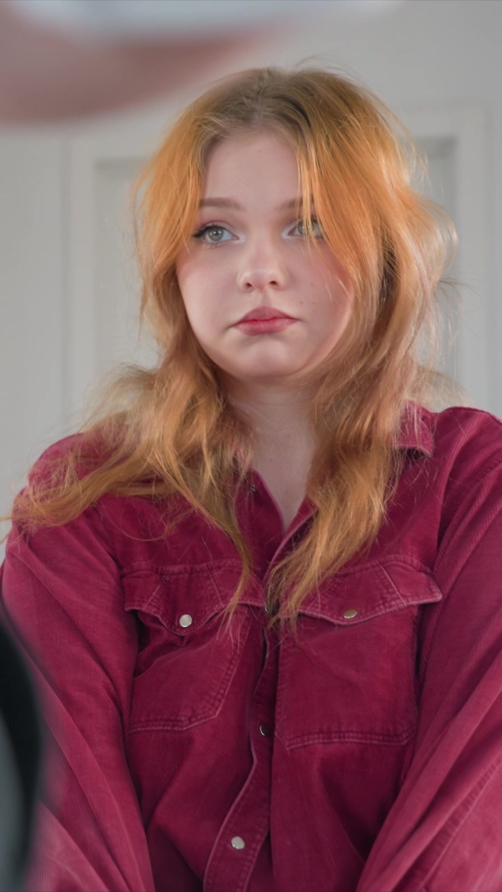 Young woman with long wavy blonde hair sits still wearing. Close up shots focus on her upper body and face highlighting. Lighting is soft throughout emphasizing natural subject