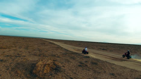 riding three-wheeler motorized trike all-terrain vehicles along a mojave desert dirt trail - slow motion