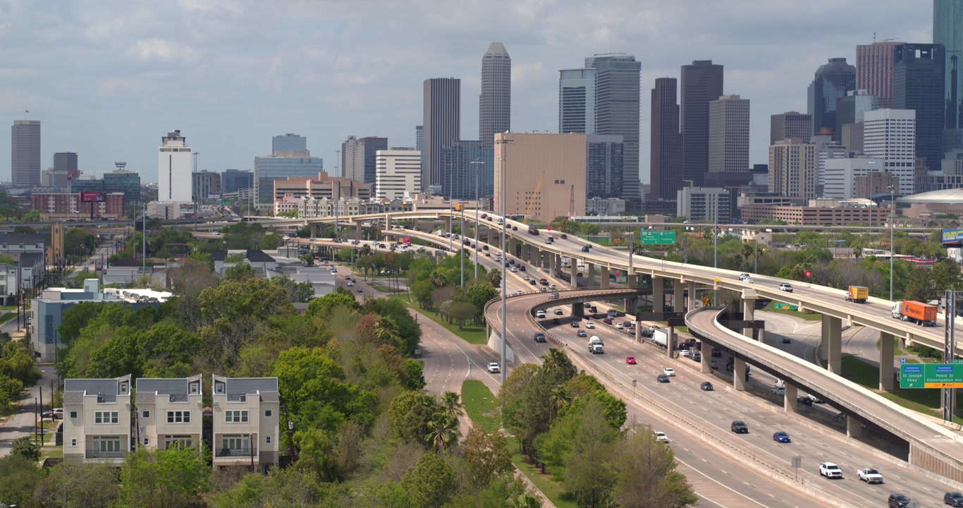 A professional establishing drone shot of cars on the I-45 South freeway (Gulf Freeway) with the downtown Houston skyline rising prominently in the background