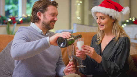 Loving-Couple-Celebrating-With-Champagne-Around-Christmas-Tree-At-Home