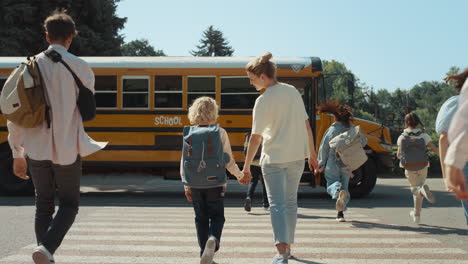 mother hold hand schoolboy walking to bus. energetic pupils running crossway.