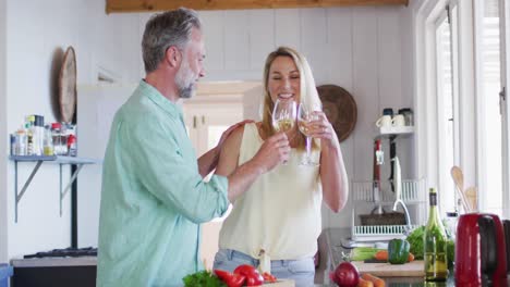 happy caucasian mature couple cooking together and drinking wine in the kitchen