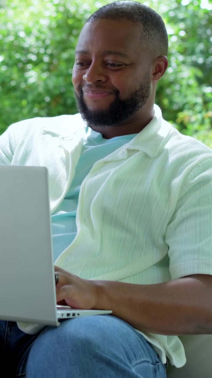 Vertical video: Man doing tech work on laptop typing and reacting to ping as camera panning garden