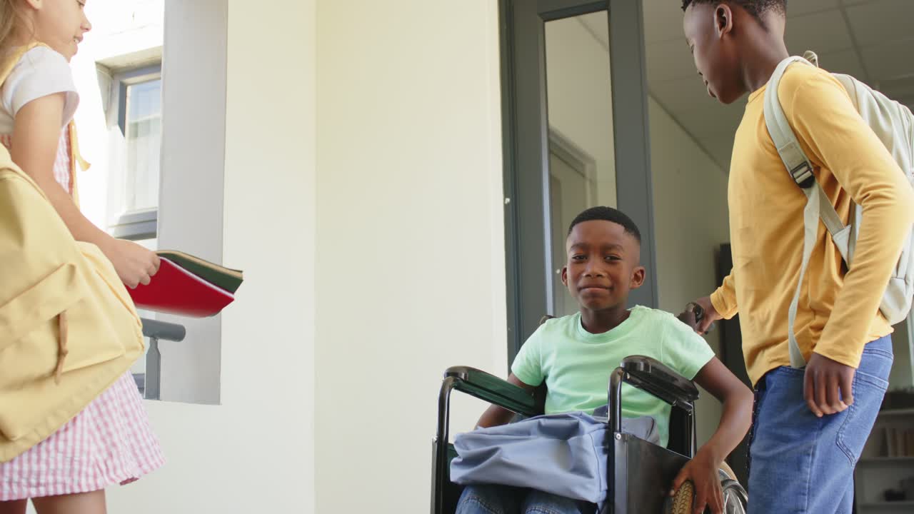 Bambini di diverse etnie in corridoio, una bambina che arriva e dà delle cartelle a un ragazzo afroamericano in sedia a rotelle per la lezione