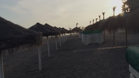 POV-walking-through-parasols-at-sunset-in-Marbella,-Malaga-beach,-shot-on-gimbal-in-4k-with-full-frame-camera