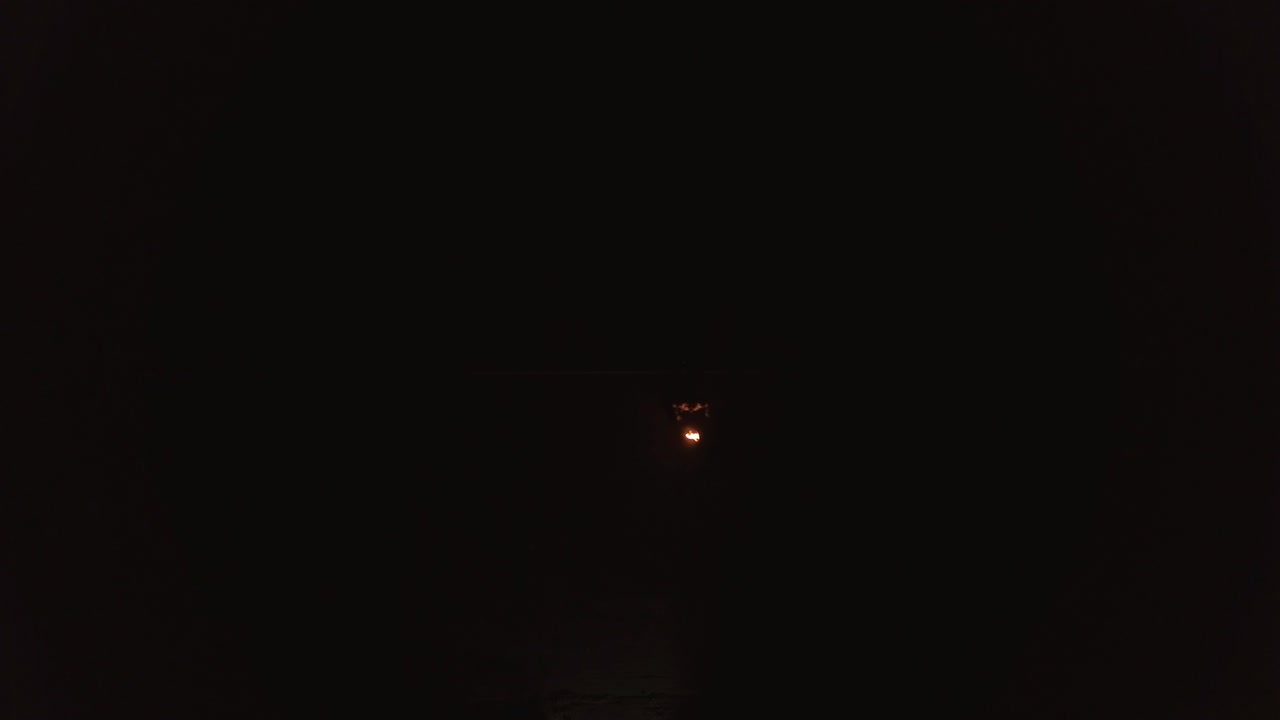 젊은 금발 남자가 밤에 공중에서 불공을 만들고 큰 불의 흐름을 호흡합니다.