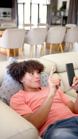 vertical video: a young biracial man is lounging on a sofa, smartphone in hand