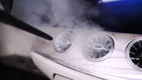 zoom fhd shot de un limpiador de vapor caliente limpiando las rejillas de ventilación del aire acondicionado en un salpicadero de coche futurista, con vapor caliente saliendo de las rejillas de ventilación