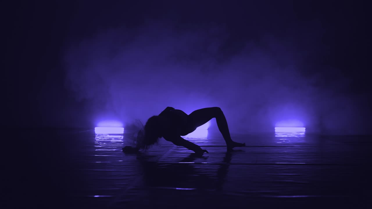 Close-up of elegant actress in black outfit performing modern contemporary dance in darkness of studio