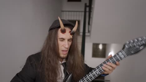 man in devil costume playing inflatable guitar
