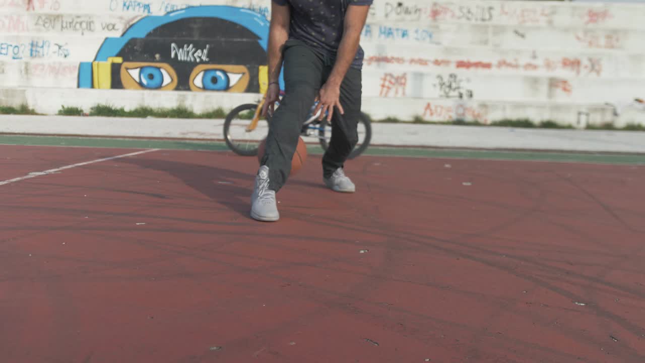 Dribbling basket ball between legs on outdoor court slow motion HD