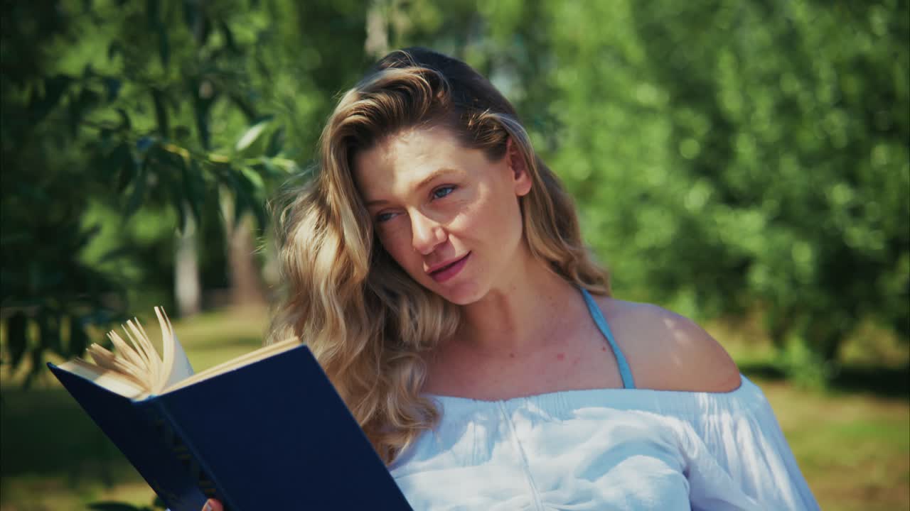 Giovane donna felice che legge un libro all'aperto in un parco soleggiato